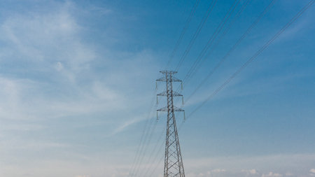 Modern high-voltage power pylon and electrical lines against a clear, expansive blue sky, representing energy, technology, and connection.の写真素材