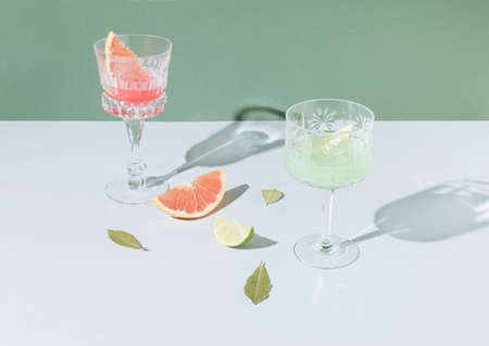 Minimal arrangement with cristal glasses and grapefruit and lime slices on the pastel green and grey background. Retro layout.の写真素材