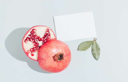 Fresh pomegranate on the pastel grey background with natural green leaves. Minimal arrangement. Creative idea.の写真素材
