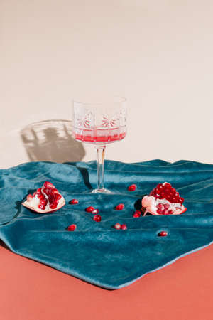 Creative arrangement  of pomegranate on a blue plush fabric. Minimal still life vintage concepet of a wine crystal glass on a pastel background.の写真素材
