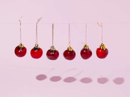 Cherry xmas baubles on a string. Creative festive idea on a pastel rosy background.の写真素材