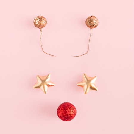 Reindeer concept made of stars, red bauble decorations and shinny antlers on pastel pink background....