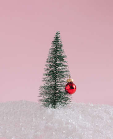 Minimal holiday idea with a christmas tree and red bauble on a snow. Holidays background.の写真素材