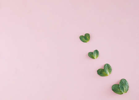 Creative layout made with green leaves hearts on a pastel pink background. Spring and love wallpaper.の写真素材