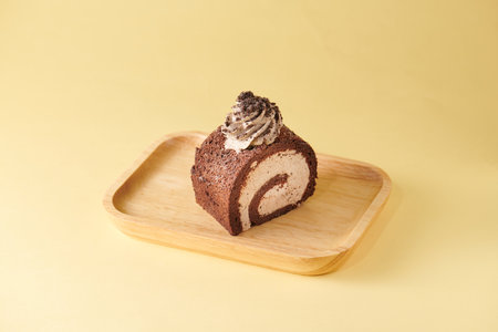 Chocolate roll cake on wooden plate on pastel yellow background.の写真素材