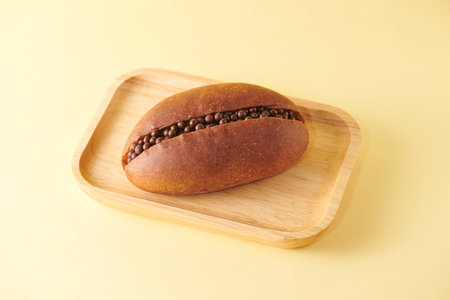 Chocolate bun on a wooden plate on a yellow background, top view