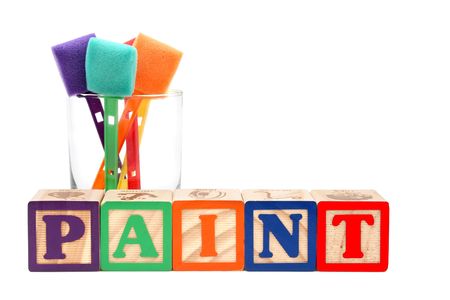 Glass of colorful paint sponges behind the word ",paint", spelt with alphabet blocks Glass of colorful paint sponges behind the word ",paint", spelt with alphabet blocks