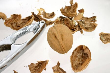 Silver nut cracker laying next to whole and cracked walnuts.