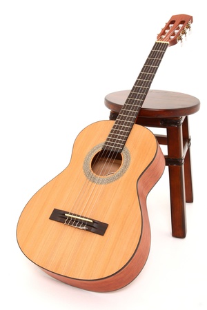 Child size acoustic guitar leaning against a wooden stool over white background.の写真素材