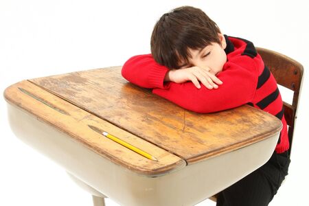 Adorable 7 year old boy in school clothes sleeping in desk over white background.の写真素材