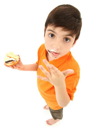 Attractive 8 year old boy standing with donut and cake licking food off fingers.の写真素材