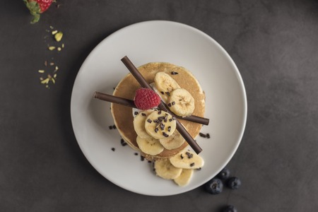 Pancakes with strawberries, raspberries, banana, chocolate and cream on a white plate. Horizontal. Copyspace. Top viewの写真素材
