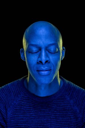 Black man with eyes closed. Studio photo with blue light isolated on black background. Concentration or peace concept. Verticalの写真素材