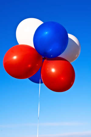 A bunch of party balloons in patriotic colors in the sunshine against a blue sky.の写真素材