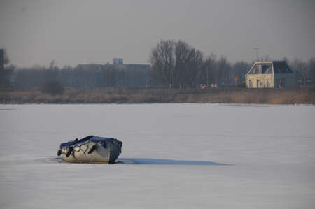 A small boat is lying on a frozen canal near Amsterdam, the Netherlandsの写真素材
