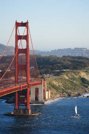A little boat sails underneath the Golden Gate Bridge, San Francsico, during sunet.