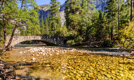 A classic stone bridge over Merced river on a sunny summers afternoon, flowing through Yosemite Valley. Yosemite National Park, California.の写真素材