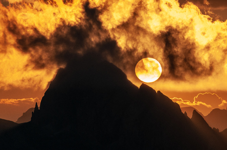 A closeup of the setting sun behind a mountain at the Passo di Giau, in the Italian Dolomites, on a late July evening.の写真素材