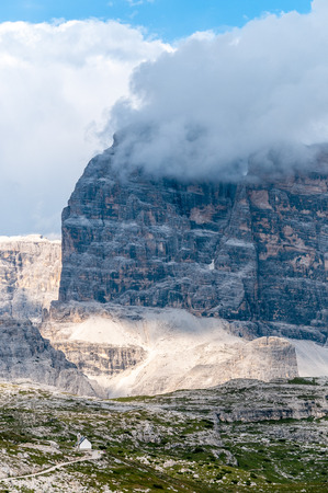 Massive granite rock face of the Mountain Ranges in Tre Cima Natural Park Area, contrasted with a little mountain chapel, in the Italian Dolomites.の写真素材