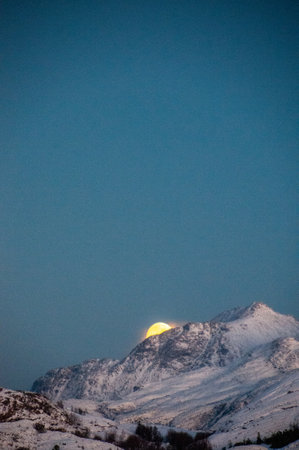 A near full moon is slowly creeping behind a mountain along the norwegian coast on an early winter morning near the town of Bodo.の写真素材