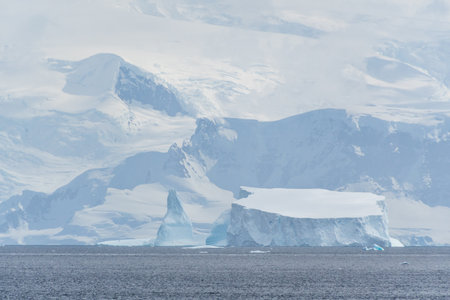 A tranquil Antarctic landscape, near Graham passage along Charlotte Bay, highlighting stark reflections, rugged mountains, and impressive icebergs.の写真素材