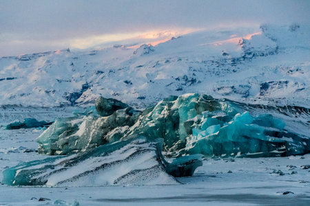 Icebergs and huge chunks for green-blueish ice fill Jokulsarlon Glacier lagoon, as the golden hour sunlight of the early morning casts a beautiful warm glow over the glacier-filled national park in Southern Iceland.の写真素材