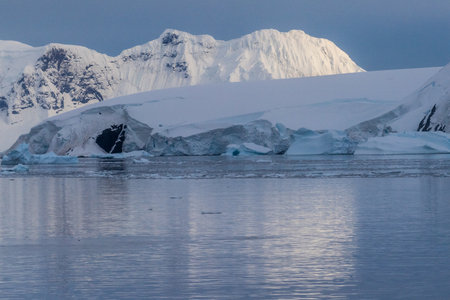 Icebergs and Glaciers align the coast of the Antarctic peninsula, and its many islands. A very tranquil sea reflects the early morning light in the Gerlache strait.の写真素材