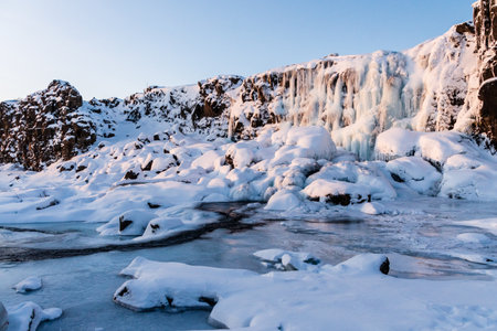 Winter outdoor scene showing a snow-covered river near the partially frozen Oxararfoss Waterfall in Thingvellir national park in the Golden circle in Iceland.の写真素材
