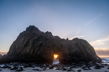 Wide-angle shot of the keyhole arch at Pfeiffer beach, California, whit the setting sun peeping through the central hole. Sunset on a winter evening in California.の写真素材