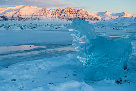 Icebergs and huge chunks for green-blueish ice fill Jokulsarlon Glacier lagoon, as the golden hour sunlight of the early morning casts a beautiful warm glow over the glacier-filled national park in Southern Iceland.の写真素材