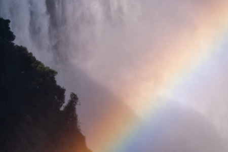 Telephoto shot of a rainbow being cast in front of the water thundering down victoria falls, in...