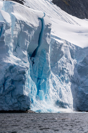 Telephoto of a giant chunk of ice calving off an ice sheet. Graham Passage, near Charlotte Bay, on the Antarctic Peninsulaの写真素材