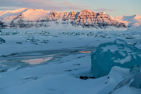 Icebergs and huge chunks for green-blueish ice fill Jokulsarlon Glacier lagoon, as the golden hour sunlight of the early morning casts a beautiful warm glow over the glacier-filled national park in Southern Iceland.の写真素材