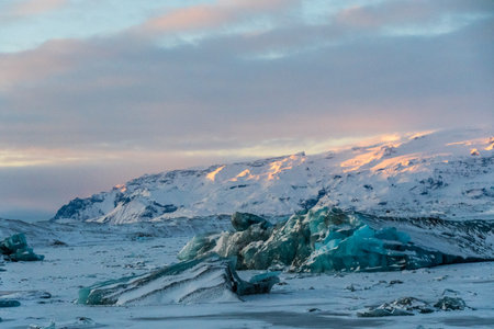 Icebergs and huge chunks for green-blueish ice fill Jokulsarlon Glacier lagoon, as the golden hour sunlight of the early morning casts a beautiful warm glow over the glacier-filled national park in Southern Iceland.の写真素材