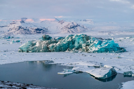 Icebergs and huge chunks for green-blueish ice fill Jokulsarlon Glacier lagoon, as the golden hour...
