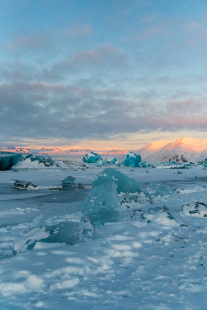Icebergs and huge chunks for green-blueish ice fill Jokulsarlon Glacier lagoon, as the golden hour...