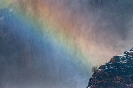 Telephoto shot of a rainbow spanning the water plunging down from victoria falls in Zimbabweの写真素材