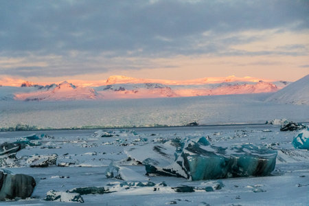 Icebergs and huge chunks for green-blueish ice fill Jokulsarlon Glacier lagoon, as the golden hour...
