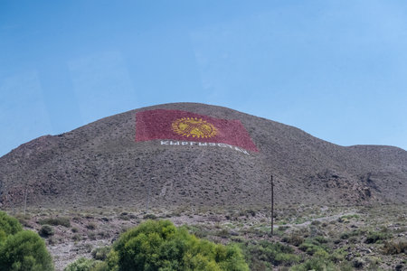 Kok-Moinok - 1, Kyrgyzstan - August 9, 2025. Road-side view of a giant Kyrgyzstan flag painted on a mountain.のeditorial素材