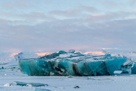 Icebergs and huge chunks for green-blueish ice fill Jokulsarlon Glacier lagoon, as the golden hour...