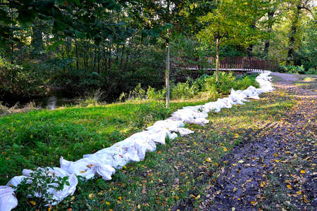 Photograph of sandbags on the shore forming a protective wall in front of a flooded streamの写真素材