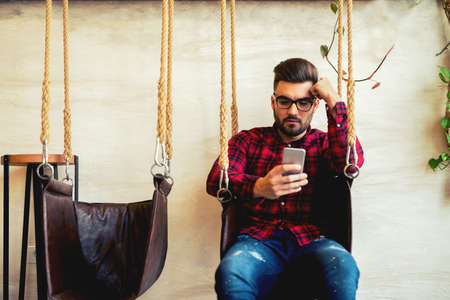 Handsome guy texting someone and sitting on the swing.