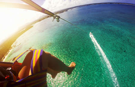 Young woman parasailing above crystal ocean water at amazing tropical island. Fisheye lens effectの写真素材