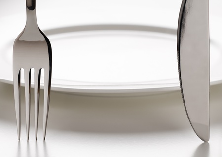 Fork and knife infront of white plate close up