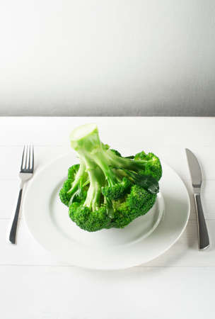 Fresh broccoli on white plate with fork and knife conceptual shootの写真素材