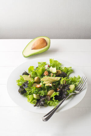 Fresh mixed green salad with avocado on white plateの写真素材