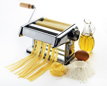 Fresh pasta cutting in machine on white backgroundの写真素材