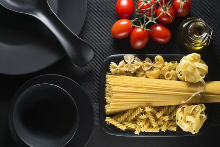 Raw pasta collection and tomatoes on black tableの写真素材
