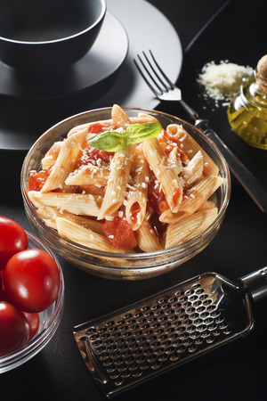 Penne pasta with tomatoes sauce and parmesan on black backgroundの写真素材