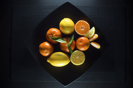 Ripe juicy tangerine, orange mandarin and lemon with leaves on black plate.の写真素材